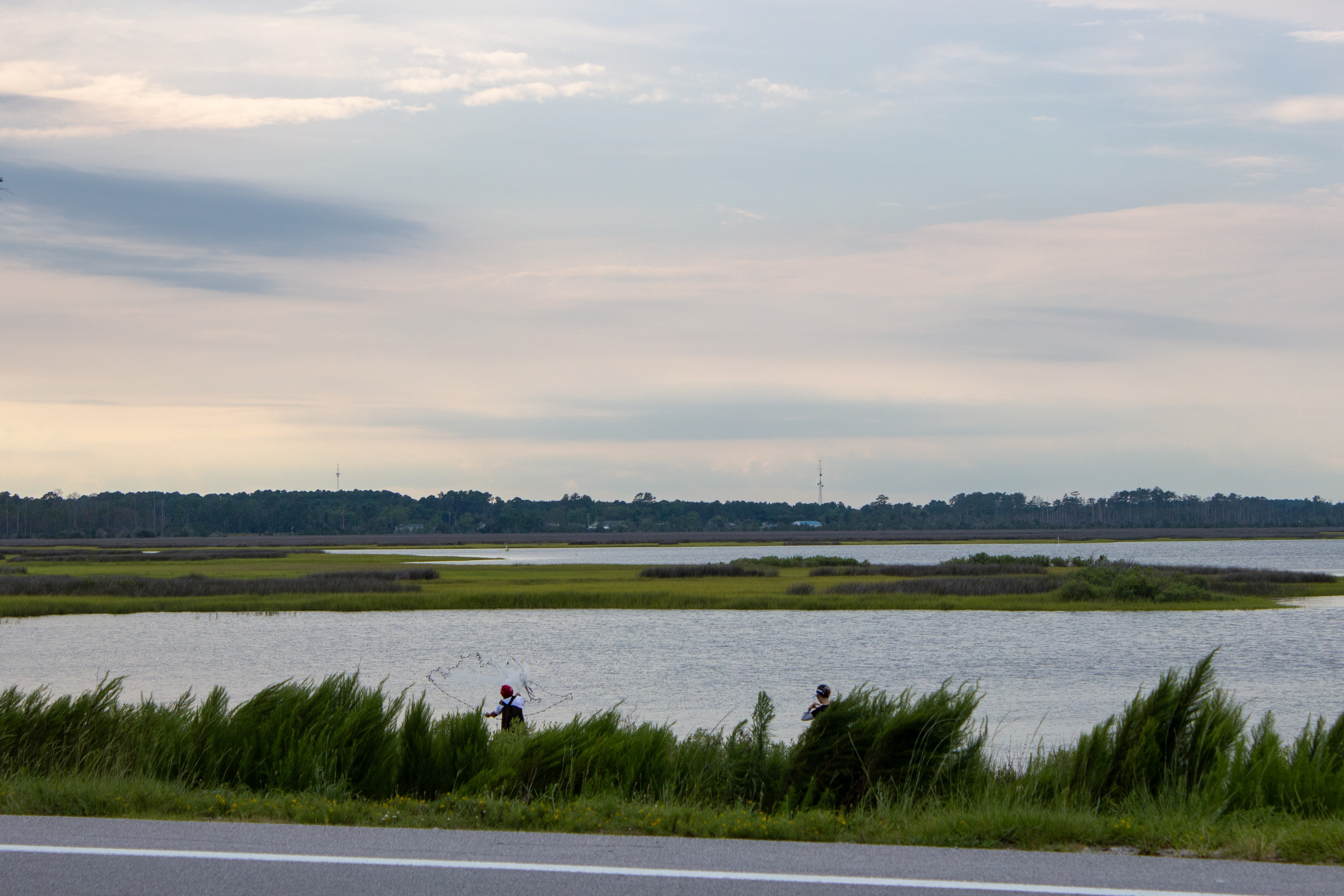 A man throws a cast net into the waters of North River on the side of US-70.