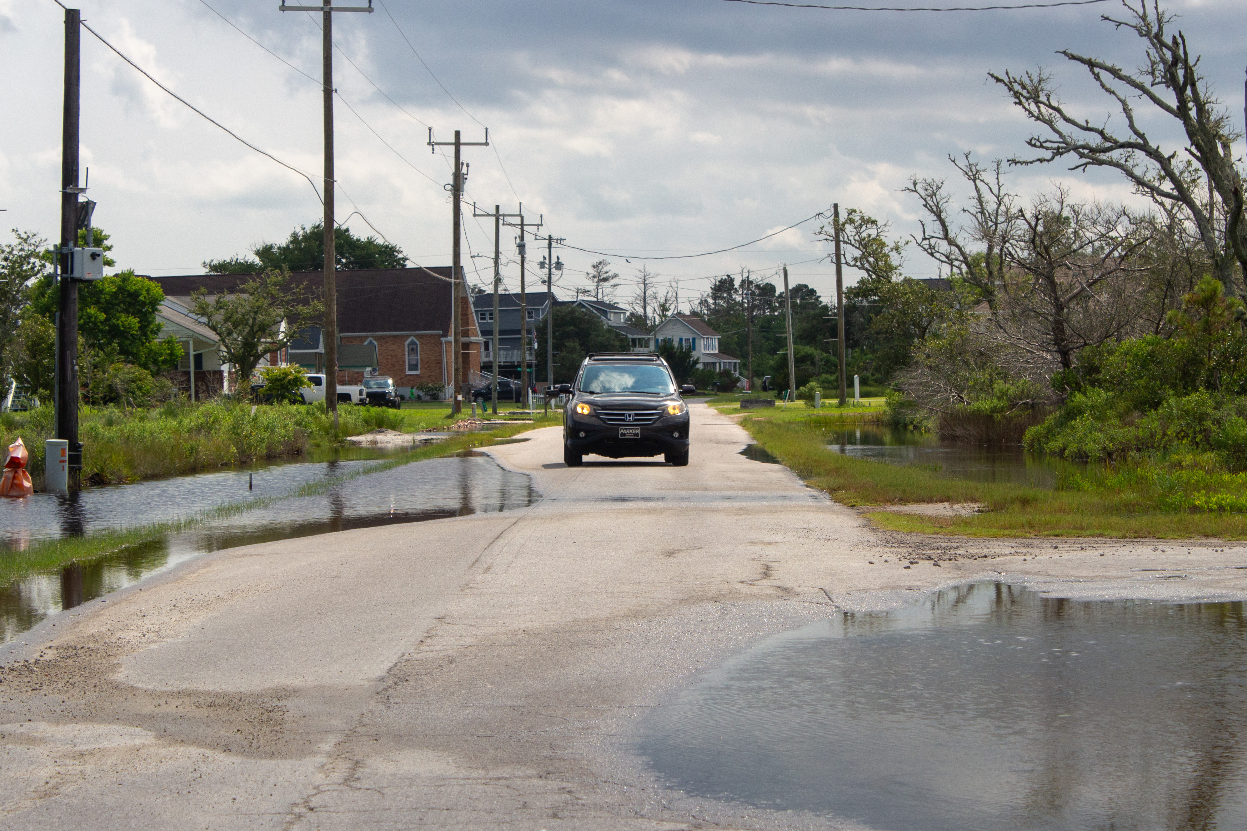 A driver avoids high-tide flooding water on a road.