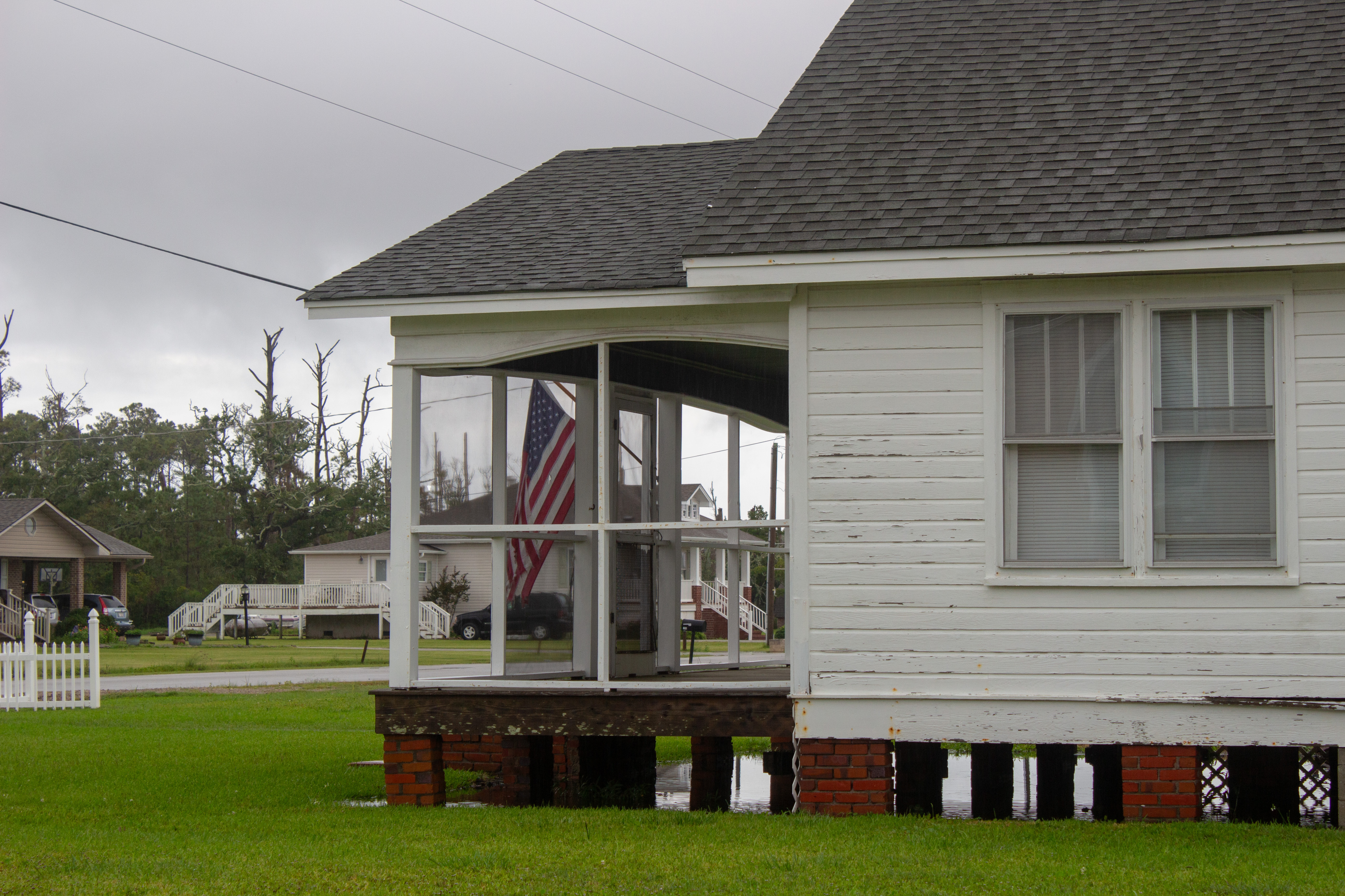 Water can be seen under a house sitting on short brick pilings.